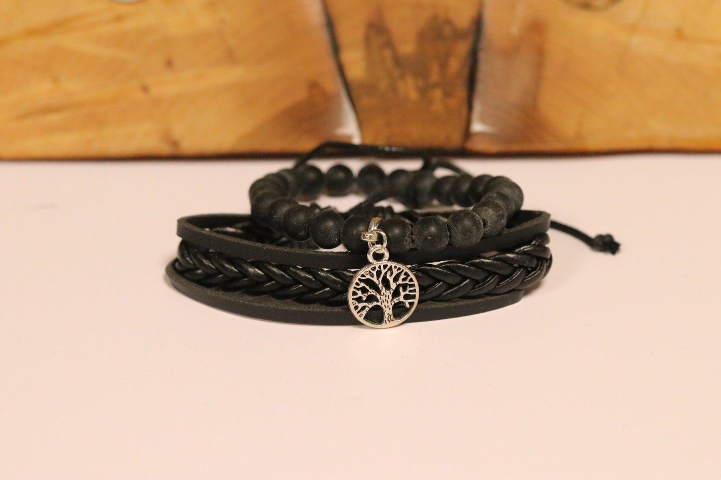Black braided bracelet with a tree of life charm on a beige surface.