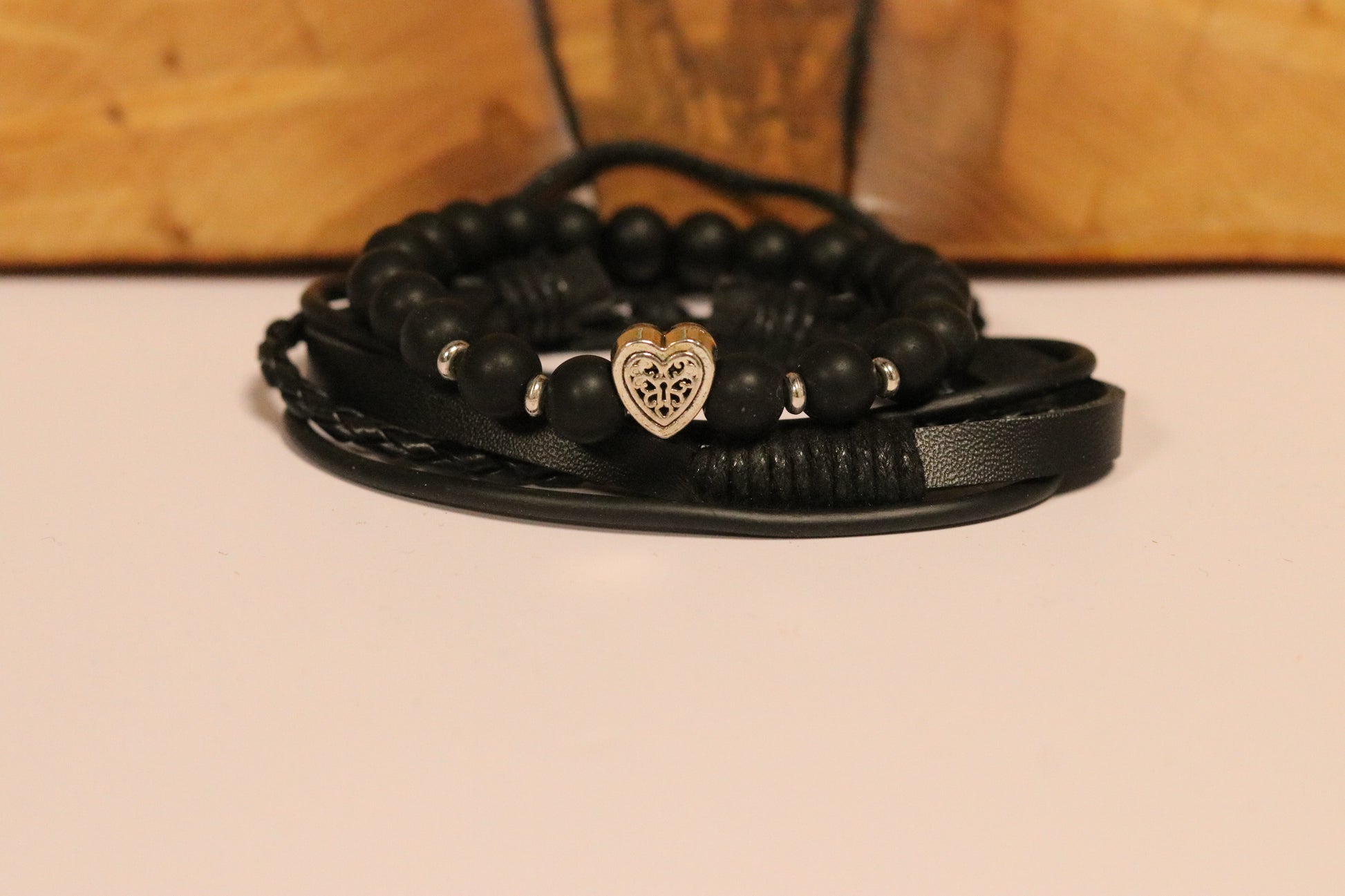 Black beaded bracelet with a heart charm on a beige surface